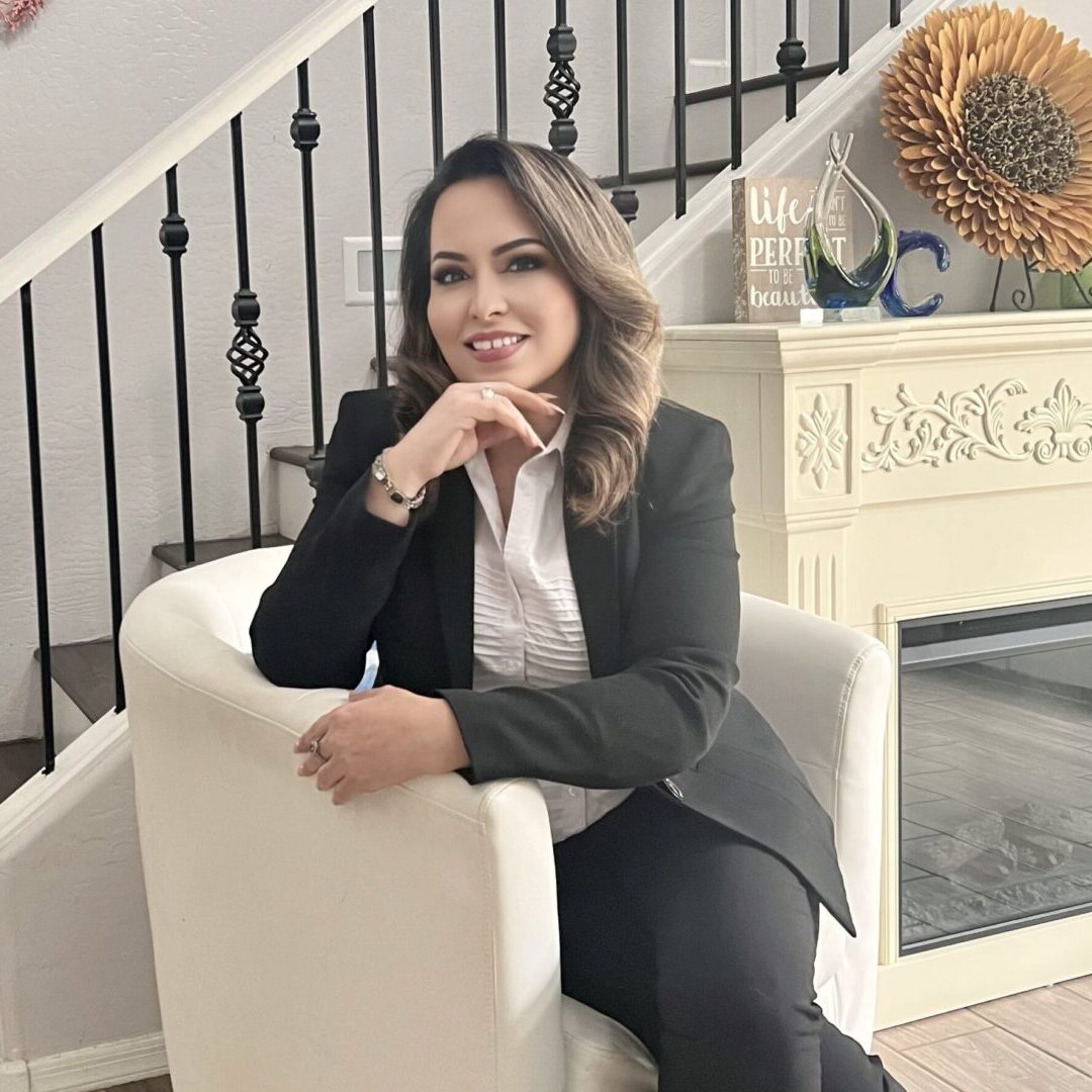 Woman in business attire sitting on a white chair indoors.